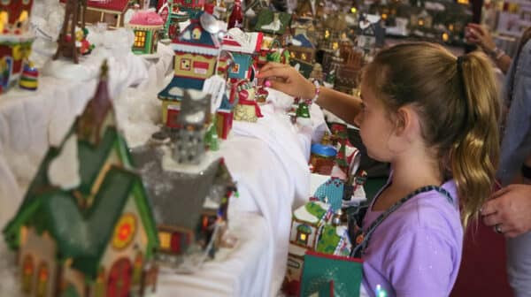 Young girl reaches out toward a display of Christmas village scenes at the Santa Claus Christmas Store
