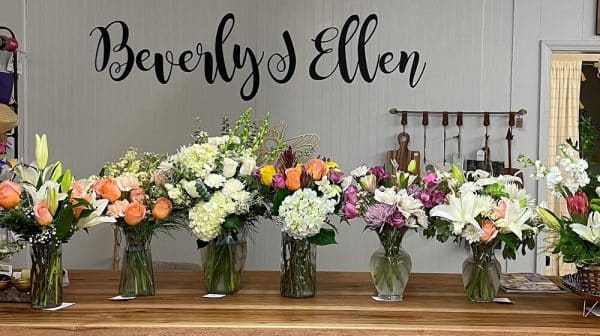 Flowers in vases are lined up side by side on the counter at Beverly J. Ellen