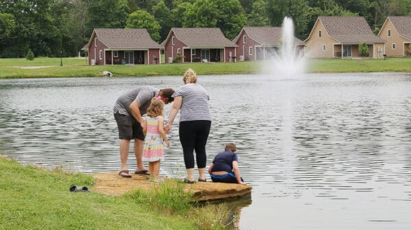 A family stands on a rock alongside a lake at Lincoln Pines Lakefront Resort with cottages shown in the background